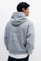 Sudadera con capucha y bolsillo canguro, confeccionada en algodón pesado con efecto lavado en tono gris claro. Presenta un estampado vertical minimalista en el pecho con números romanos y texto.