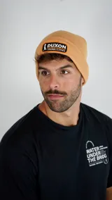 Gorro tipo beanie de punto color naranja, con parche frontal bordado con el logo de la marca Duxon.