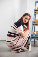 Vestido largo de tejido calado con rayas horizontales en tonos beige, marrón y amarillo. Tiene corte recto, hombros caídos, tajo lateral y logo bordado en la manga.