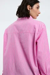 Camisa oversize de popelina a rayas celestes y blancas, con cuello camisero, manga larga con puños abotonados, cierre frontal con botones y un bolsillo en el pecho con etiqueta bordada.