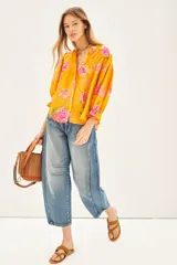 Camisa de viscosa con estampado floral en tonos amarillos y rosas. Presenta escote redondo con cierre frontal de botones, mangas al codo con terminación elástica y detalle de volado.