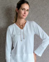 Remera blanca de manga larga con cuello en V y detalle de lazo decorativo con dije metálico en el centro del escote.