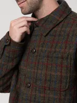 Chaqueta de hombre con estampado de tartán en tonos verde oscuro, marrón, rojo y azul. Presenta cuello camisero, cierre frontal con botones, un bolsillo de parche en el pecho y dos bolsillos laterales.