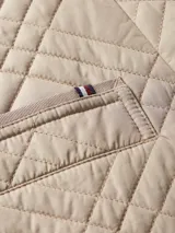 Chaquetón acolchado color beige con diseño de rombos, doble botonadura, cinturón y mangas con vuelta.