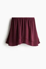 Pollera mini de doble capa en tejido con leve brillo color bordó, con cintura estándar con elástico fino y bajo ondulado con vuelo.