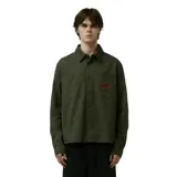 Camisa de manga larga color verde militar, con cuello clásico, cierre de botones frontales, dos bolsillos en el pecho y un parche ovalado con texto en rojo en el bolsillo izquierdo.