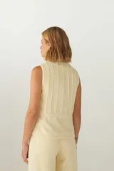 Chaleco corto entallado de lana fina sin teñir, color marrón claro jaspeado, con cierre frontal y alforzas verticales en delantera y espalda.