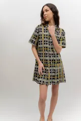 Vestido camisero corto con estampado a cuadros en tonos verde, azul y rojo. Presenta cuello camisero, mangas corta, cierre frontal con botones y falda tableada de corte bajo.
