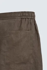 Bermuda de lino color blanco hueso, de corte relajado y tiro medio. Presenta cintura elástica ajustable con cordón, pliegues frontales y bolsillos laterales y trasero.