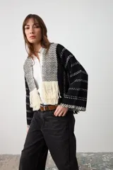 Chaqueta abierta de tejido de punto con diseño geométrico en blanco y negro. Presenta solapas con patrón de espiga y terminaciones con flecos largos en el frente. Posee mangas anchas con detalle de líneas horizontales punteadas.