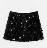 Minifalda negra de fiesta con base de lentejuelas y aplicaciones circulares de distintos tamaños, de tiro alto y caída suelta.