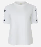 Blusa blanca de algodón con cuello redondo y mangas cortas abullonadas. Presenta pequeños bordados en color azul marino distribuidos en las mangas.