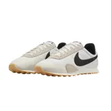 Championes Nike modelo Pre Montreal Racer Vintage, con diseño retro de perfil bajo. Presenta una base de tela técnica blanca con refuerzos de gamuza en tono gris claro en la puntera y el talón. Incluye el logo de Nike en color negro en los laterales y suela de goma con relieve para mayor tracción.
