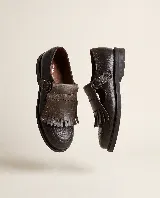 Mocasín de cuero natural color marrón, con costuras visibles, hebilla lateral metálica y solapa desmontable con flecos.