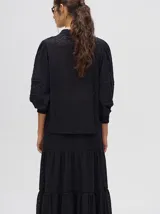 Camisa de broderie de algodón color negro, con diseño de calados, cuello mao con cierre de botones, mangas abullonadas con puños fruncidos y detalles de galones con transparencias.