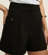 Short sastre de cintura alta con estructura definida, bolsillos laterales decorados con tachuelas metalizadas y recortes delanteros con costura aparente.