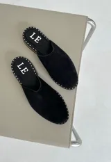Mules de cuero negro con tachas plateadas en el borde de la suela y plantilla con logo estampado.