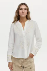 Camisa blanca de lino con cuello mao, manga larga y delicados bordados en tono tostado en el pecho y los puños.