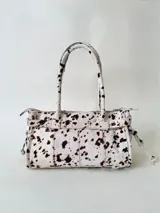 Cartera de cuero de tamaño medio con estructura rígida. Presenta una tira decorativa con tachas y hebillas metálicas en los extremos, además de lazos laterales. Cuenta con doble asa para llevar al hombro y cierre superior.