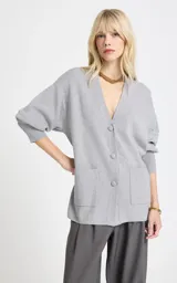 Cardigan de punto color gris, de corte holgado, con escote en V profundo, cierre frontal de botones, mangas largas con puños ajustados y bolsillos delanteros aplicados.