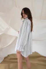 Camisa de manga larga, estilo oversize, con cuello camisero y puños fruncidos con elástico. Presenta un estampado de rayas verticales finas en tonos blanco, celeste y azul oscuro.