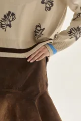 Sweater de punto color bordó con diseño de flores estampadas en tono crema, cuello redondo y puños con detalle de franjas en contraste. Presenta un bordado pequeño en el pecho.