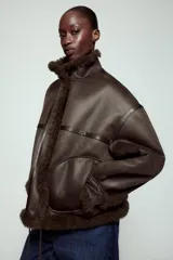 Chaqueta bomber de cuello alto con forro interior de pelo sintético. Presenta cierre frontal con botones, bolsillos delanteros y bajo ajustable con cordones.