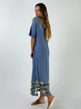 Vestido midi de tejido ligero color beige, con cuello en V, mangas cortas y ruedo decorado con aplicaciones de crochet en tonos tierra y rosado.