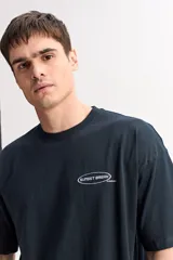 Remera boxy de algodón color negro, con diseño estampado en la espalda que incluye texto y el logo de la marca.