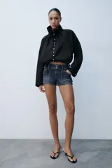 Cazadora de algodón negra con cuello subido ajustable con lazadas, manga larga, bolsillos de vivo en los laterales y bajo ajustable con cordones. Cierre frontal con botones.