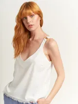 Top blanco con escote en V, breteles anchos con argollas de madera y ruedo con flecos.