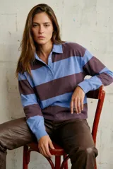 Sweater tipo polo de algodón, con diseño de rayas horizontales anchas en tonos azul y marrón. Presenta cuello camisero con cierre frontal de tres botones y mangas largas con puños ajustados.