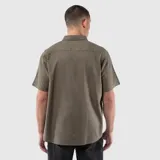 Camisa de manga corta con cuello clásico, cierre frontal de botones y un bolsillo en el pecho. Presenta un diseño de corte regular con textura natural.