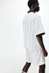 Short de fútbol blanco en malla, modelo de corte relajado con cintura elástica ajustable mediante cordón, bolsillos laterales y líneas negras decorativas en los laterales. Cuenta con el logo de Lotto estampado en contraste en una pierna.