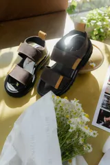 Sandalias marrones con tiras de cuero con ajuste de velcro y detalles en amarillo.