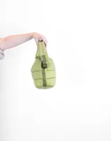 Bolsito tipo tote acolchado de color amarillo, con diseño de líneas horizontales y logo de la marca estampado en el frente. Cuenta con dos asas superiores acolchadas y una correa ajustable de cinta en color beige.