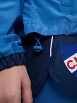 Campera deportiva Umbro del Club Nacional de Football, modelo Sky para mujer. Diseño en tonos azul marino y celeste con detalles en blanco y líneas finas rosadas, cuello alto, cierre frontal y bolsillos.
