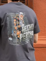 Remera gris de manga corta con gran estampado en la espalda de un jugador de rugby lastimado con muletas y la frase "Hecho Percha".