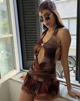 Vestido corto de estilo cut-out con estampado abstracto en tonos tierra. Presenta un escote halter profundo con un aplique metálico en forma de estrella de mar en el centro y una falda con volados en el ruedo.