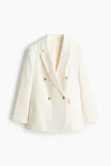 Blazer levemente largo color blanco con solapas de muesca, botones delanteros, hombreras y bolsillos delanteros ribeteados con solapa. Diseño cruzado y forrado.