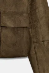 Cazadora corta color marrón de efecto ante, con cuello solapa, manga larga y bolsillos de plastrón con solapa en el delantero. Cierre frontal con botones.