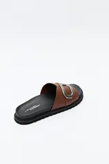 Sandalia slide color beige con hebilla metálica plateada y suela negra.