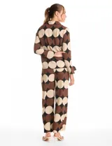 Conjunto de dos piezas compuesto por camisa de manga larga con nudo frontal y pantalón estilo palazzo de pierna ancha. Ambas prendas presentan un estampado geométrico de círculos grandes en tonos marrón, negro y beige. La camisa cuenta con cuello solapa y cierre frontal con botones, mientras que el pantalón posee tiro alto y corte holgado.