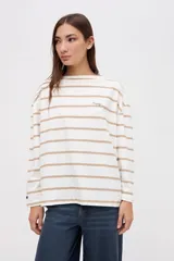 Remera de manga larga con diseño a rayas horizontales en color crema y rojo. Presenta un corte holgado, cuello redondo y un pequeño bordado en el pecho.