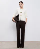 Chaqueta de hilo color crema con cuello redondo, mangas largas y cierre frontal con botones dorados. Diseño calado de crochet en la parte delantera y trasera.