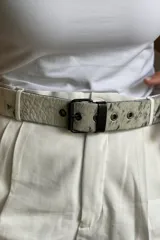 Cinturón de cuero con textura de pelo animal en tono blanco con manchas negras, hebilla metálica negra y pasador de cuero liso.