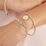 Brazalete tipo esclava de alambre redondo en plata 925, con dije de medalla circular colgante.