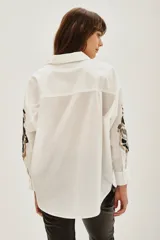 Camisa blanca de algodón con mangas largas, destacada por bordados decorativos en color negro y plateado en las mangas.