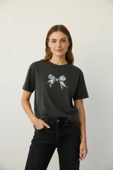 Remera de algodón color gris oscuro, de corte holgado y manga corta, con cuello a la base y estampa frontal de un moño con detalles de strass.