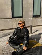 Campera de estilo bomber combinada en denim negro y mangas de cuero sintético, con cierre frontal y bolsillos con cremallera en el pecho.